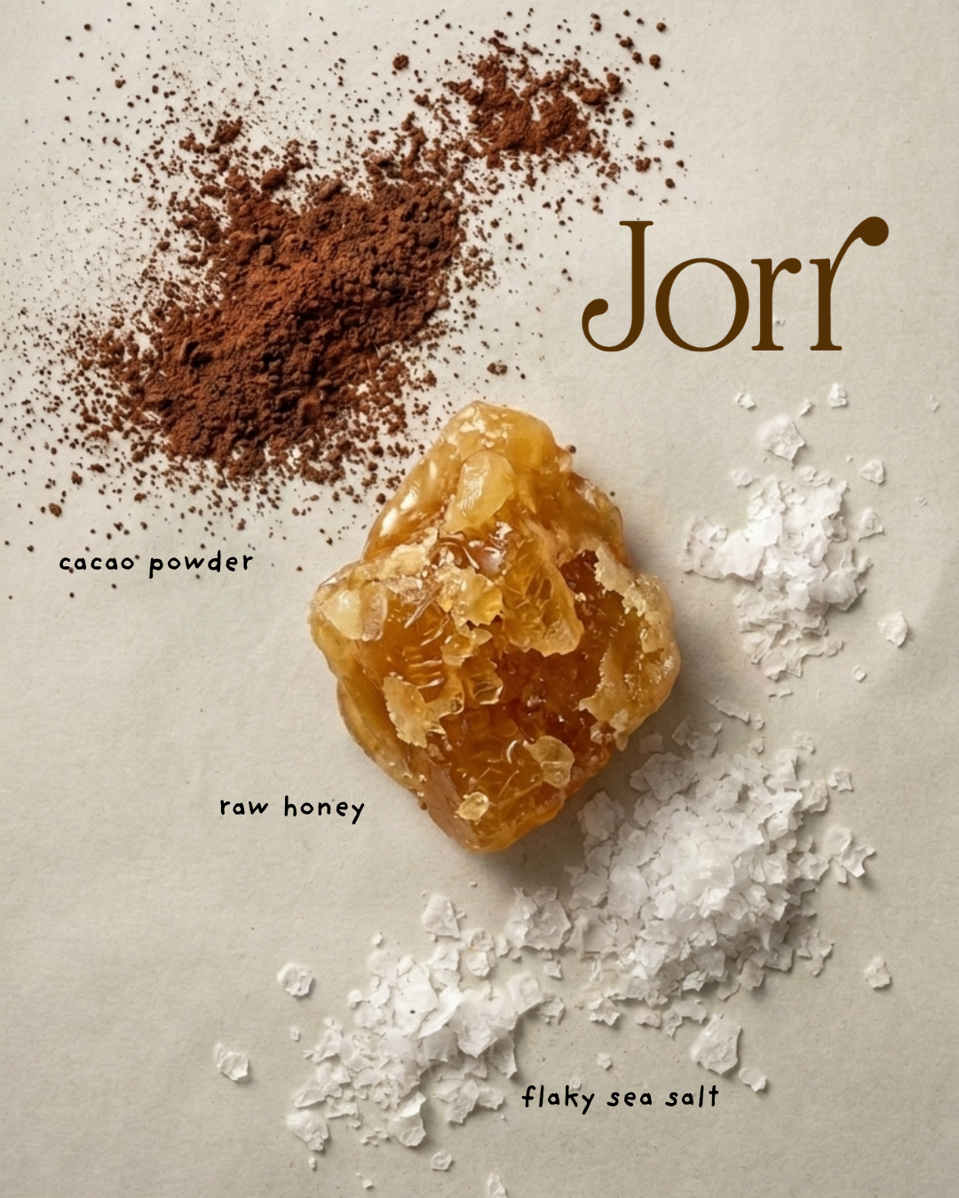 A styled flat-lay of a raw honey crystal surrounded by labeled ingredients: cacao powder, raw honey, and flaky sea salt, on a light beige background with the brand name Jorr at the top right.
